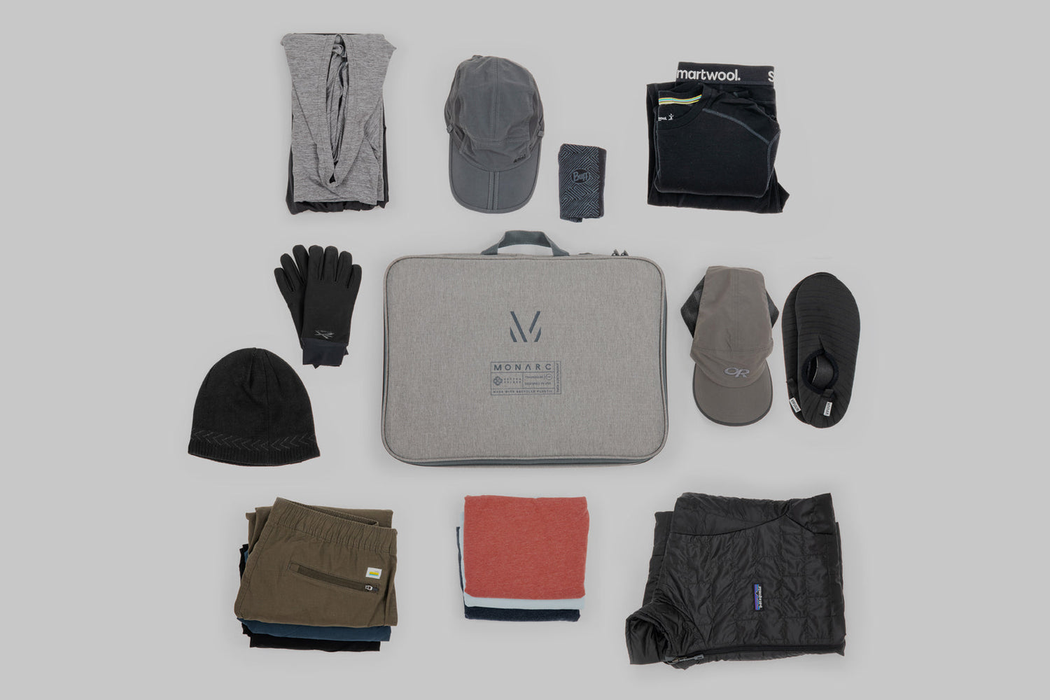 Carefully curated Monarc travel gear layout on a neutral background, featuring a gray travel organizer