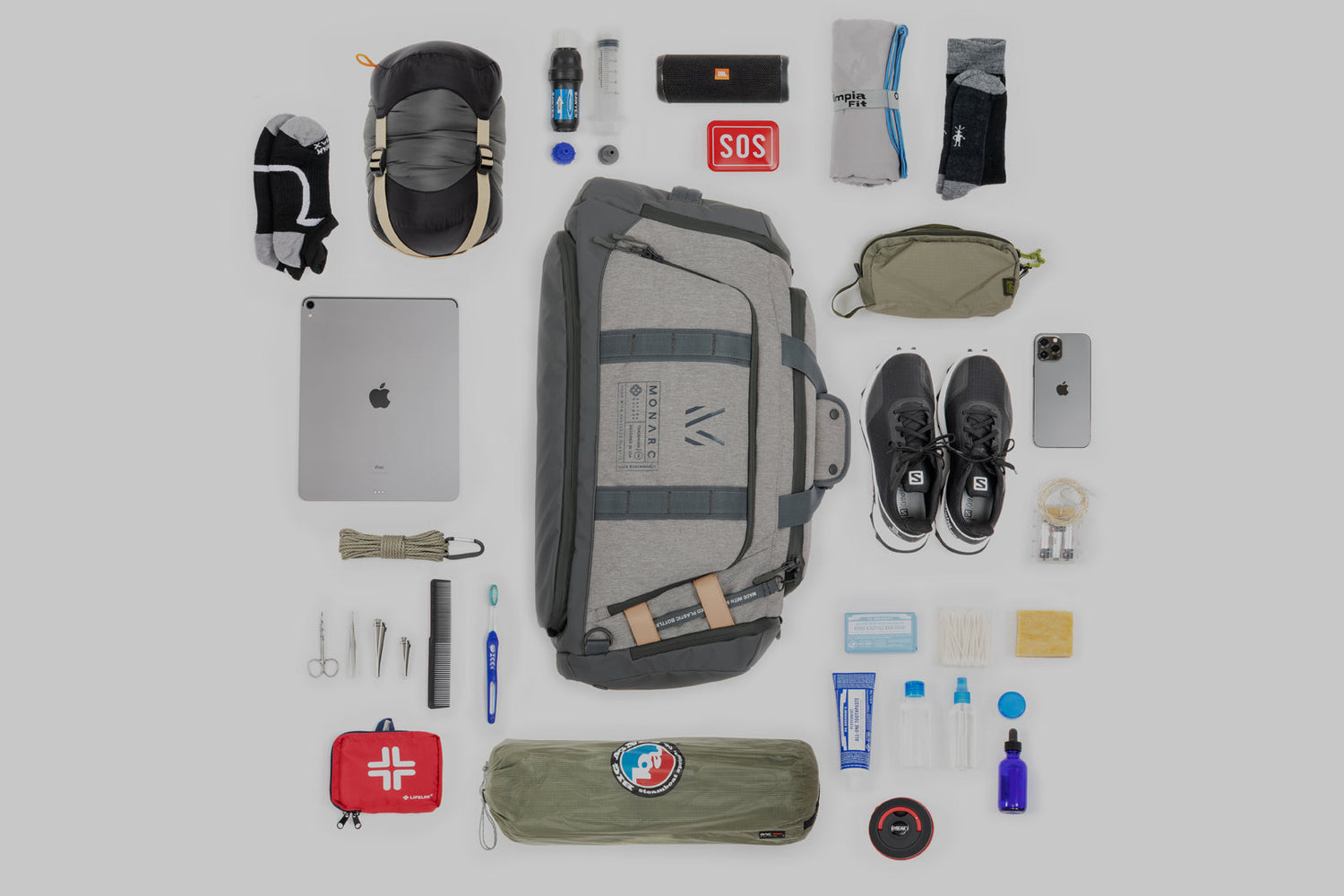 Carefully curated Monarc travel gear layout on a neutral background, featuring a gray duffel backpack