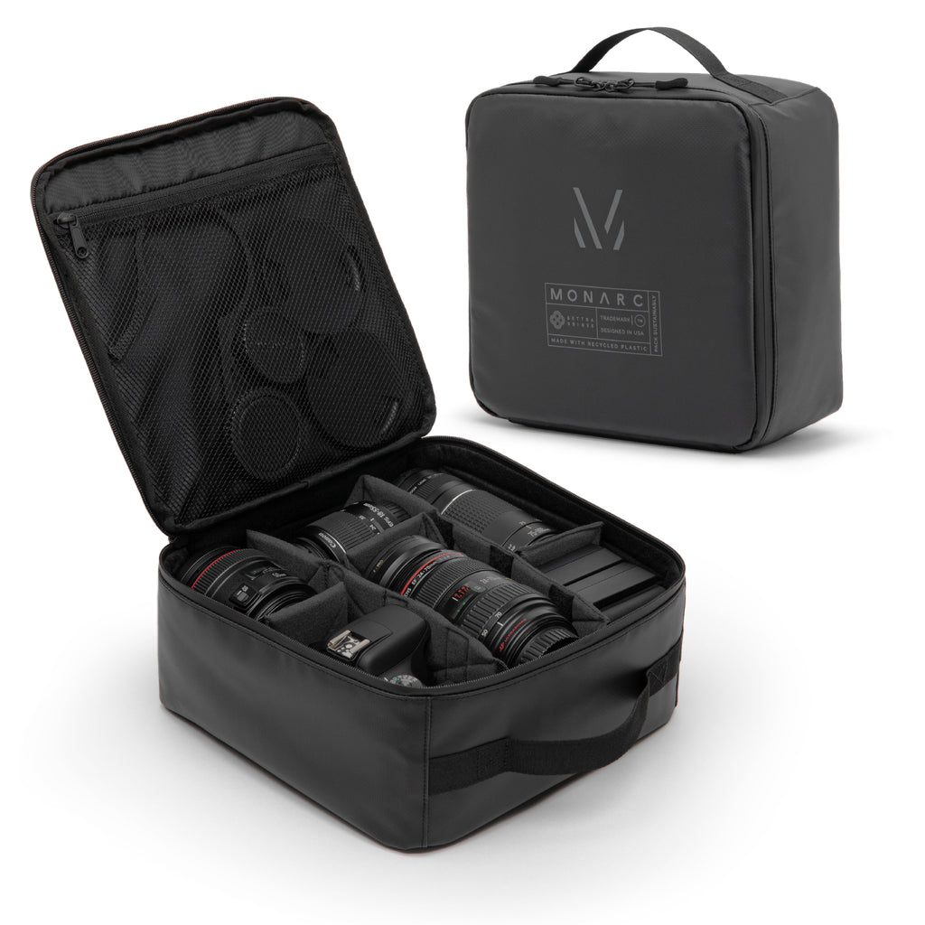 Monarc Camera Cube open to display its organized storage compartments filled with various camera lenses and accessories. The cube is crafted from durable, water-resistant material made with recycled plastic, featuring a compact, protective design with a UV printed Monarc logo.