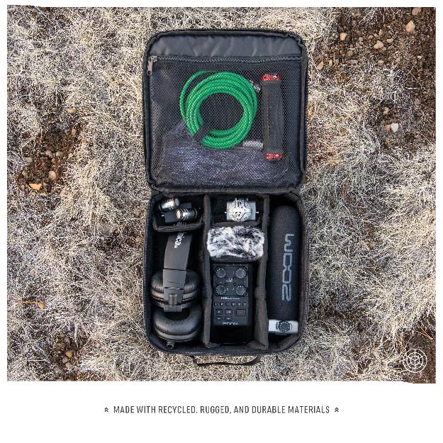 Outdoor shot of the Monarc Camera Cube open on the ground, showing its storage capabilities for various audio recording equipment including microphones, cables, and a digital recorder. The camera cube's interior is neatly organized to protect and secure the gear, made from recycled, durable materials suited for rugged environments.