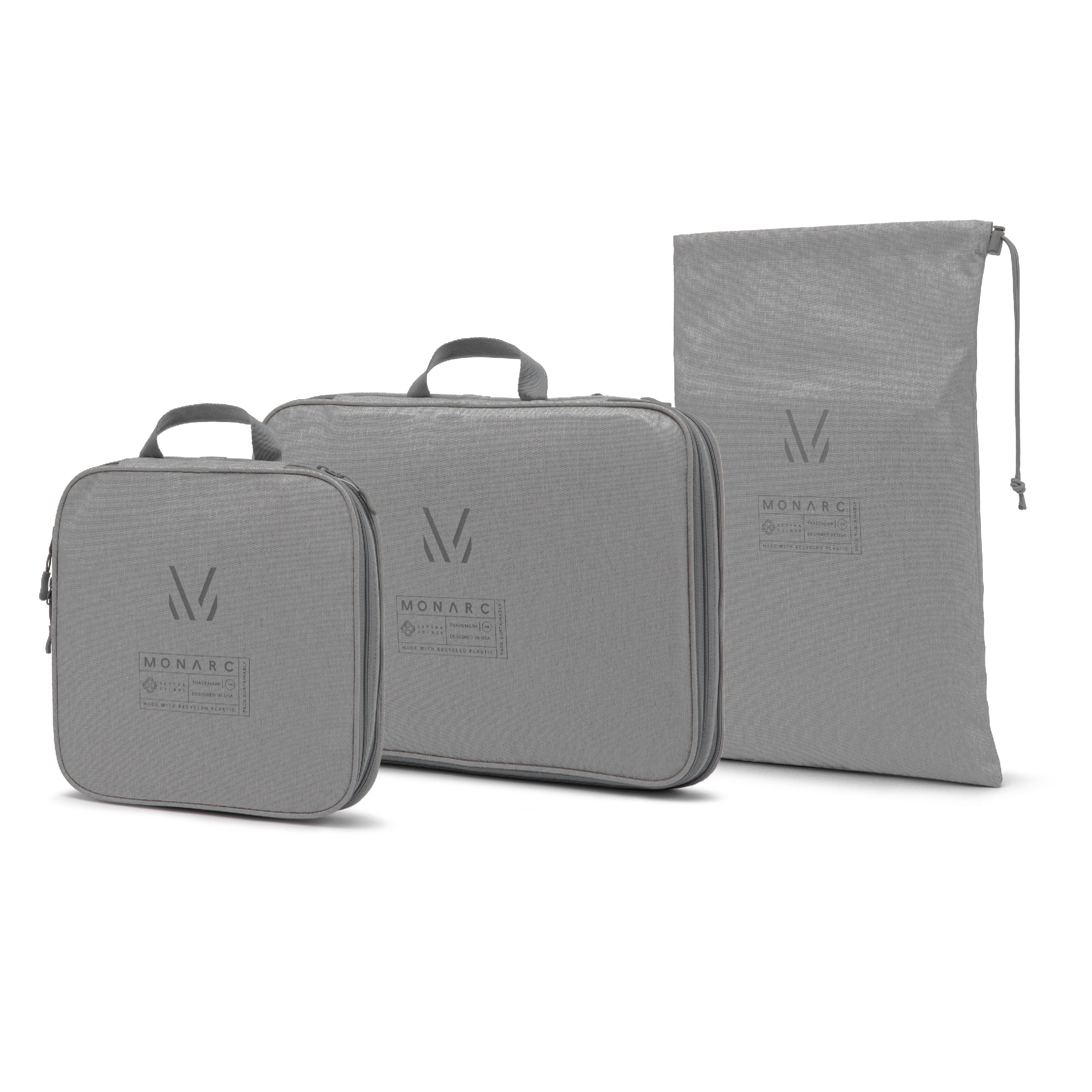 Versatile Monarc travel set featuring two packing cubes and a laundry bag in stylish gray, each marked with the iconic Monarc logo. The packing cubes are designed for efficient organization, offering compact and adaptable storage solutions for travelers, while the laundry bag ensures separation and cleanliness of garments. All items are made from durable, water-resistant recycled materials.